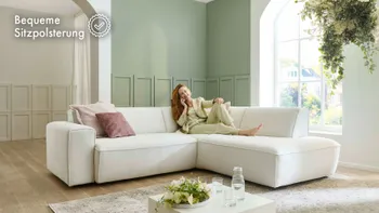 Frau entspannt auf einem hellen Ecksofa in modernem Wohnzimmer mit grünen Wänden und großen Fenstern, stilvolles Ambiente